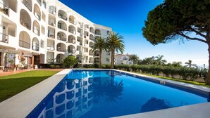 A swimming pool with a clear blue water surface, surrounded by a well-maintained lawn and palm trees. - 'Sea Views Nice Sunset Sun' Apartment with Sea View, Shared Pool, and Wi-Fi (Nerja)