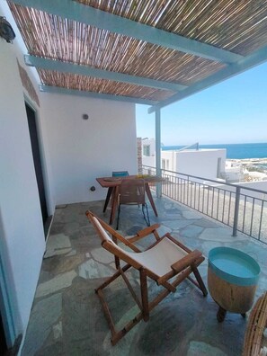 Ein überdachter Außenbereich mit Tisch und Stühlen, einem Steinboden und Blick auf das Meer.