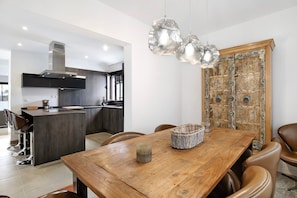 Una cocina moderna con una isla central, un comedor con mesa de madera y sillas de cuero, y una puerta de madera decorativa.