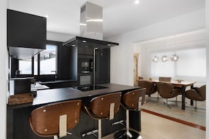 Een moderne keuken met een centraal eiland, barstoelen en een eethoek met een tafel en stoelen.