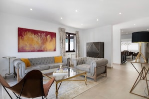 Een moderne woonkamer met een grijze bank, een glazen salontafel en een bruine leren fauteuil.