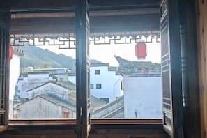 A traditional Chinese window with intricate lattice design, offering a view of a mountainous landscape and traditional buildings.