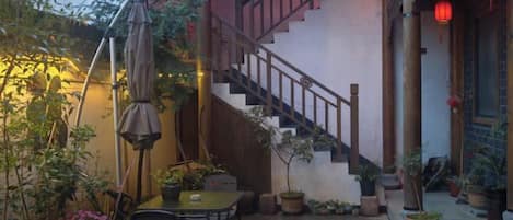 Un escalier menant à un niveau supérieur, une table avec des chaises et des plantes en pot dans une cour.
