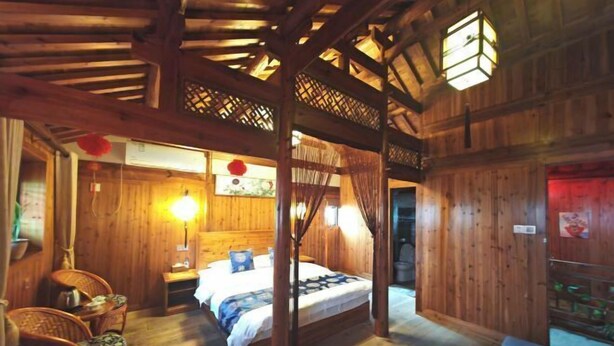 A wooden room with a bed, a chair, a table, and a hanging light fixture.