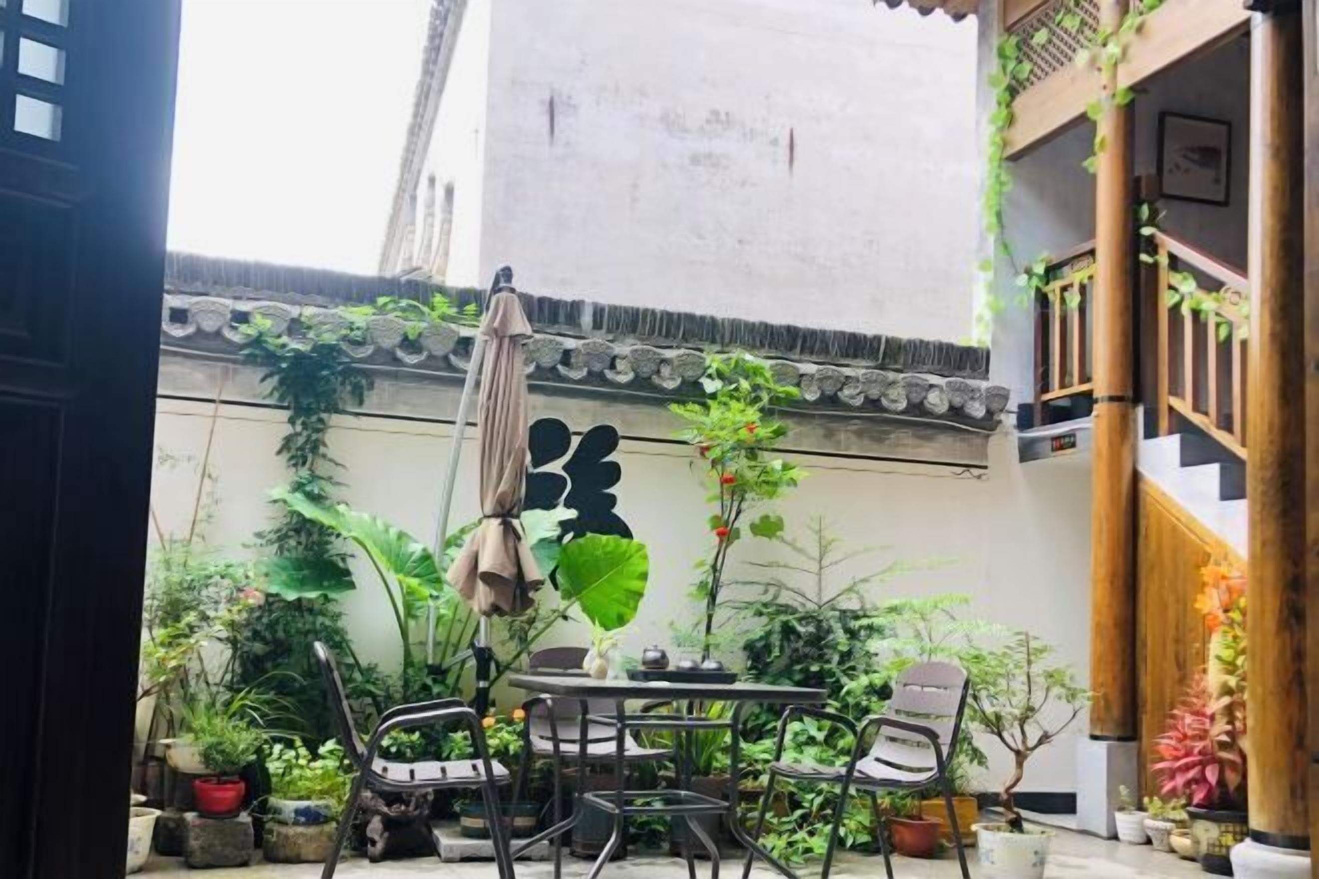 A courtyard with a table and chairs, surrounded by potted plants and a traditional architectural wall.