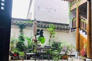Une cour avec une table et des chaises, entourée de plantes en pot et d’un mur d’architecture traditionnelle.