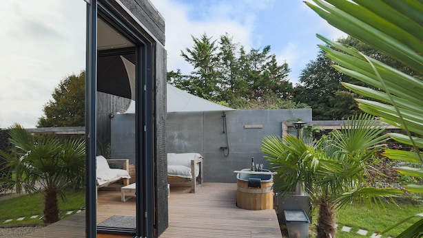 Une terrasse extérieure moderne avec une plateforme en bois, un jacuzzi et un coin salon agrémenté d’une serviette blanche.