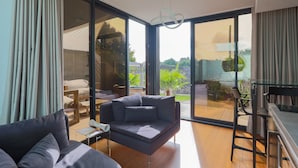 Un salon moderne avec un canapé, une petite table et un fauteuil. Une porte-fenêtre coulissante donne accès à un espace extérieur agrémenté d’un jardin.