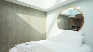 Une chambre à coucher moderne avec un puits de lumière, un grand miroir rond et un lit parfaitement fait.