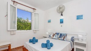 Ein Schlafzimmer mit Bett, Nachttischen, einem Fenster mit Vorhängen, einem Ventilator und Wandbildern.
