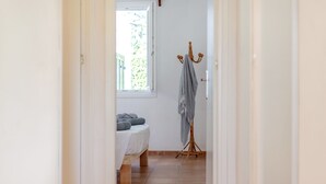 Ein schmaler Flur mit einem Bett, einem Wäscheständer und einem Fenster mit Blick auf Grünflächen.