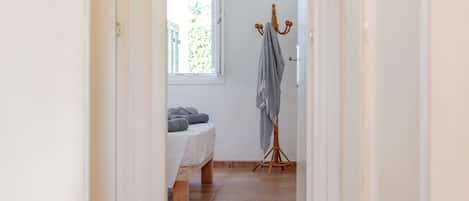A narrow hallway with a bed, a drying rack, and a window with a view of greenery.