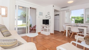 Ein modernes Wohnzimmer mit einer Couch, einem Fernseher, einem Essbereich und einer Glasschiebetür, die auf eine Terrasse führt.