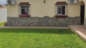 Una casa con techo de tejas, pared de piedra y dos ventanas con rejas.