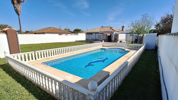 Una piscina rectangular con barandilla blanca, rodeada por un muro blanco y un césped cuidado.