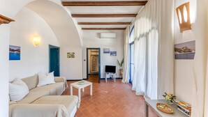 A room with a sofa, a small table, a TV, and a window with curtains. - Villa 'Blu La Cambusa' with Shared Pool, Wi-Fi and Air Conditioning (Castro)