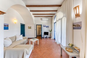 Ein Zimmer mit einer Couch, einem kleinen Tisch, einem Fernseher und einem Fenster mit Vorhängen.