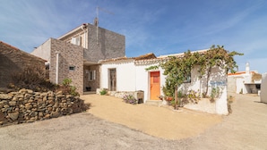 A rustic building with a stone wall, a small garden, and a clear sky.