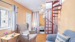 A compact room with a bed, a chair, a small table with cups, a window, and a red spiral staircase.