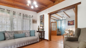 A living room with a sofa, armchair, wooden flooring, and a door leading to another room. - Holiday Home "El Llanete" with Mountain Views, Shared Pool & Wi-Fi (Vega de San Mateo)