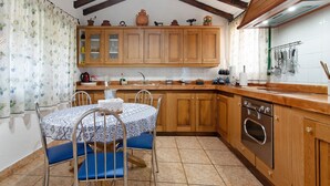 A kitchen with wooden cabinets, a dining table with chairs, and a hanging rack with utensils. - Holiday Home "El Llanete" with Mountain Views, Shared Pool & Wi-Fi (Vega de San Mateo)