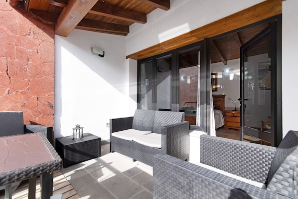 An outdoor patio area with wicker furniture, a tiled floor, and a brick wall.