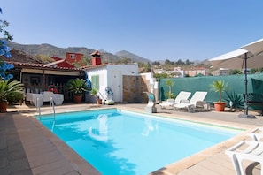 A swimming pool with lounge chairs, a lifeguard chair, and a stone wall.