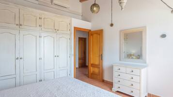 Un dormitorio con cama, armario, cómoda, espejo y lámpara colgante.