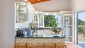 A kitchen with white cabinets, a large island with bar stools, and a view through the glass doors. - Holiday Home 'Can Juan Pedro' with Sea View, Wi-Fi and Air Conditioning (Formentera)