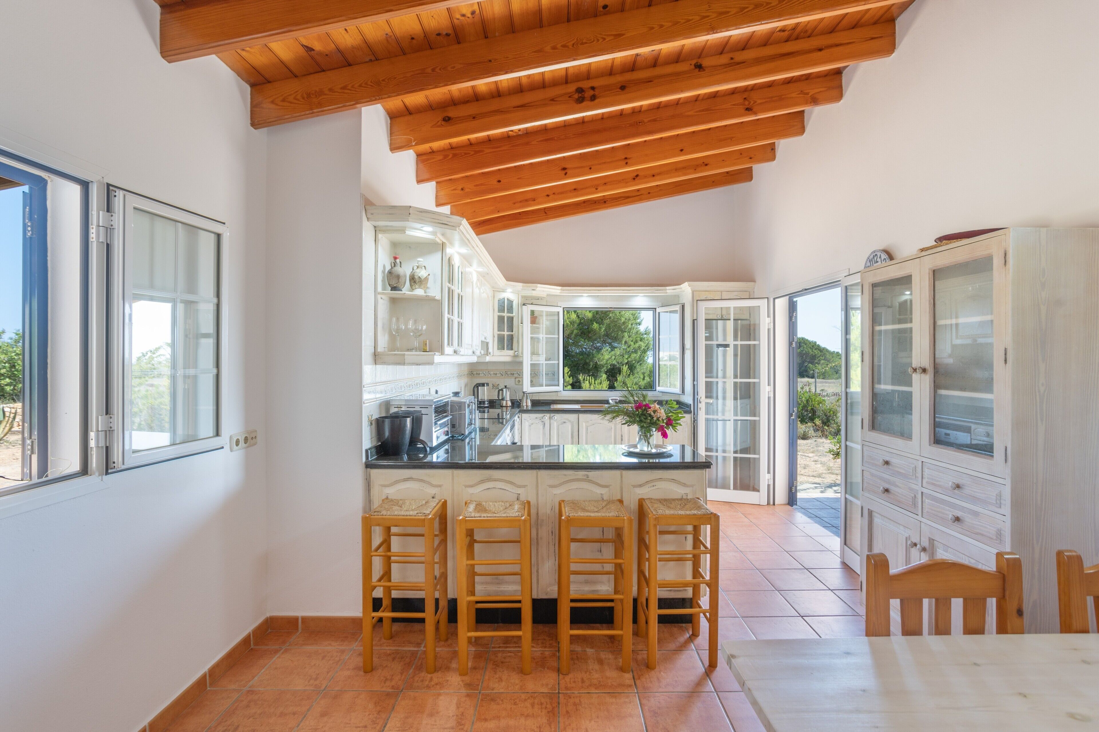A kitchen with a central island, wooden stools, and a view to the outside.