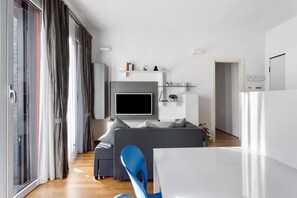 A modern living room with a flat-screen TV, grey sofa, blue chair, and a dining area. - Holiday Apartment "La Casetta Di Ale" with 2 Balconies & Wi-Fi (La Spezia)