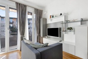 A modern living room with a grey sofa, a flat-screen TV, a glass shelf with decorative items, and a sliding glass door to an outdoor balcony. - Holiday Apartment "La Casetta Di Ale" with 2 Balconies & Wi-Fi (La Spezia)