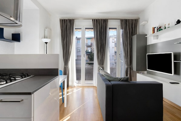 A modern kitchen with a gas stove, a dining table, and a sofa in a living area with a TV. - Holiday Apartment "La Casetta Di Ale" with 2 Balconies & Wi-Fi (La Spezia)