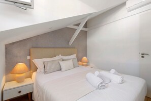 Quarto com cama, mesas de cabeceira, abajur e porta.