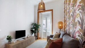 Un salon moderne doté d’un téléviseur à écran plat, d’un meuble de rangement en bois, d’un canapé gris, de rideaux à motifs et d’un luminaire suspendu.