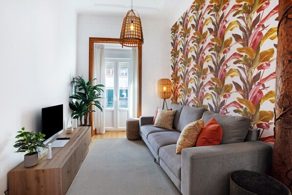 Ein modernes Wohnzimmer mit einem grauen Sofa, einem HolztV-Möbel, einer großen Topfpflanze und einer Wand mit Muster.