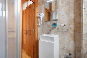 Ein Badezimmer mit Holztür, Waschbecken in Weiß, Spiegel und Handtrockner.