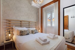 Ein Schlafzimmer mit einem hölzernen Kopfteil, einem Nachttisch mit Lampe, einem Spiegel und ordentlich gefalteten Handtüchern auf dem Bett.