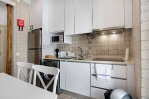 A modern kitchen with white cabinets, a stainless steel refrigerator, a microwave, a sink, and a washing machine.