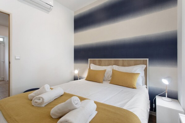 A hotel room with a bed, two bedside lamps, and a wall with a gradient design. - Apartment "Casa Ribeiro - Maresia" with Wi-Fi & A/C (Nazaré)