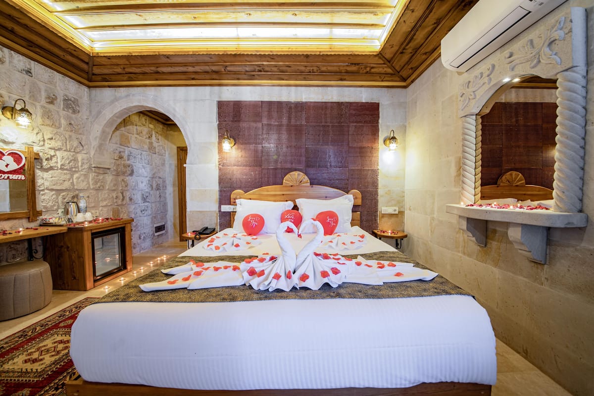 Una habitación de hotel con una cama grande, paredes de piedra, vigas de madera y una chimenea de piedra.
