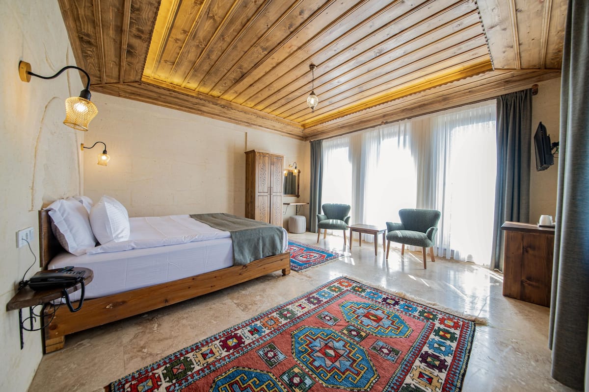 Un dormitorio con techo de madera, una cama, un escritorio, una silla y un tapete estampado.