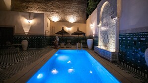 An indoor swimming pool with a blue water feature, surrounded by patterned tile flooring and walls, and decorative umbrellas. - Riad Fes Ziyat & Spa (Fes)