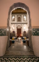 Un interior con un arco central, baldosas decoradas y una zona de estar con mesas y sillas.
