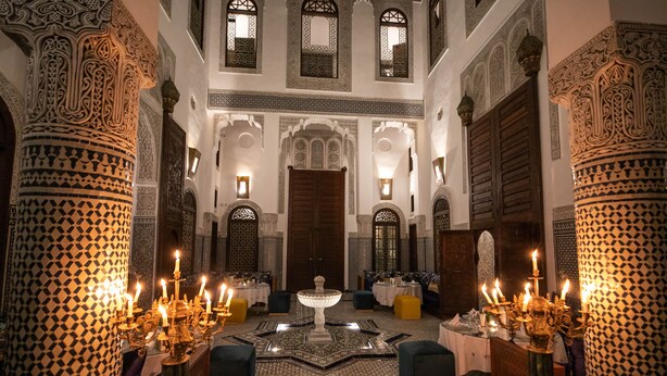 An ornate interior with intricate tile work, a central fountain, and candle-lit tables. - Riad Fes Ziyat & Spa (Fes)