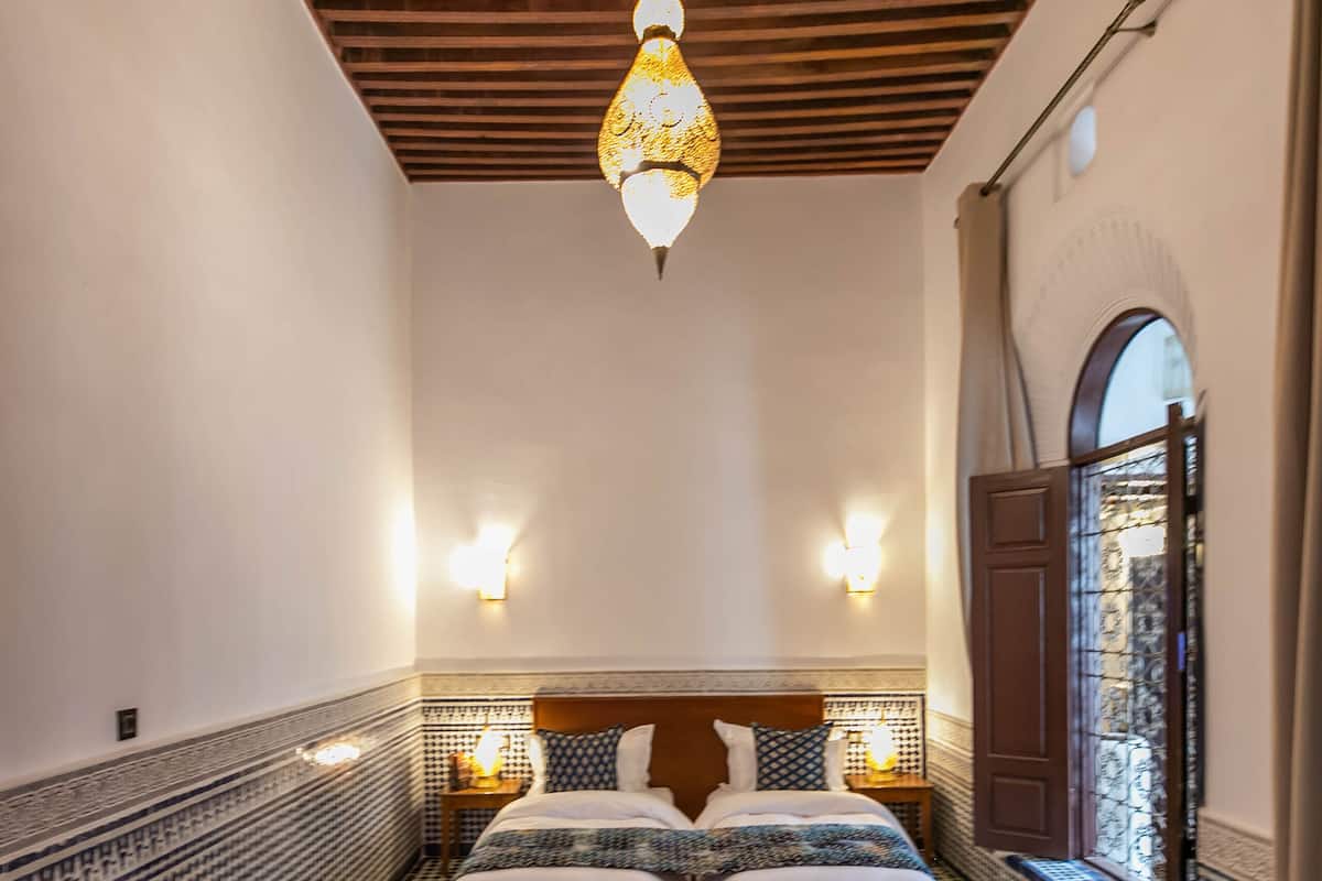 A room with a bed, a blue sofa, a tray with a drink, and patterned floor tiles.