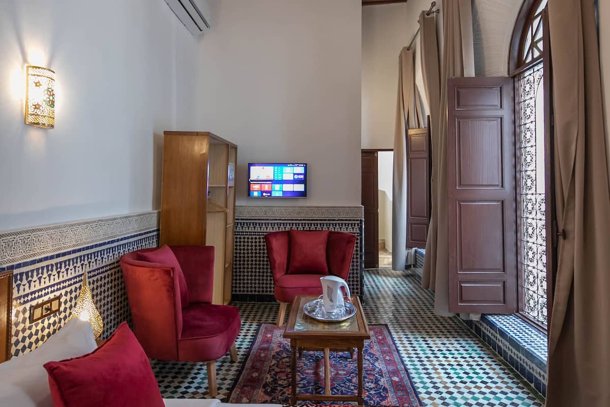 A hotel room with a bed, red chairs, a television, and a patterned floor.