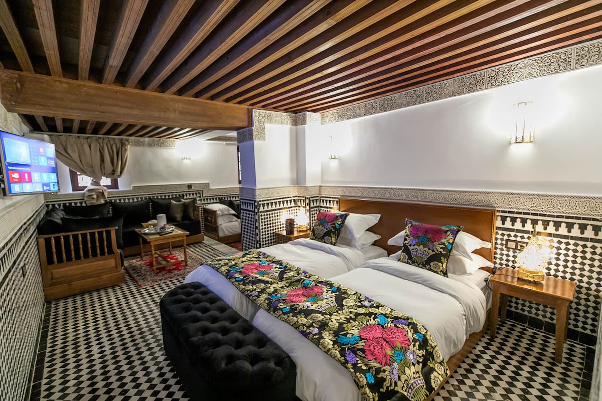 A hotel room with a large bed, a sofa, a TV, and a patterned floor.