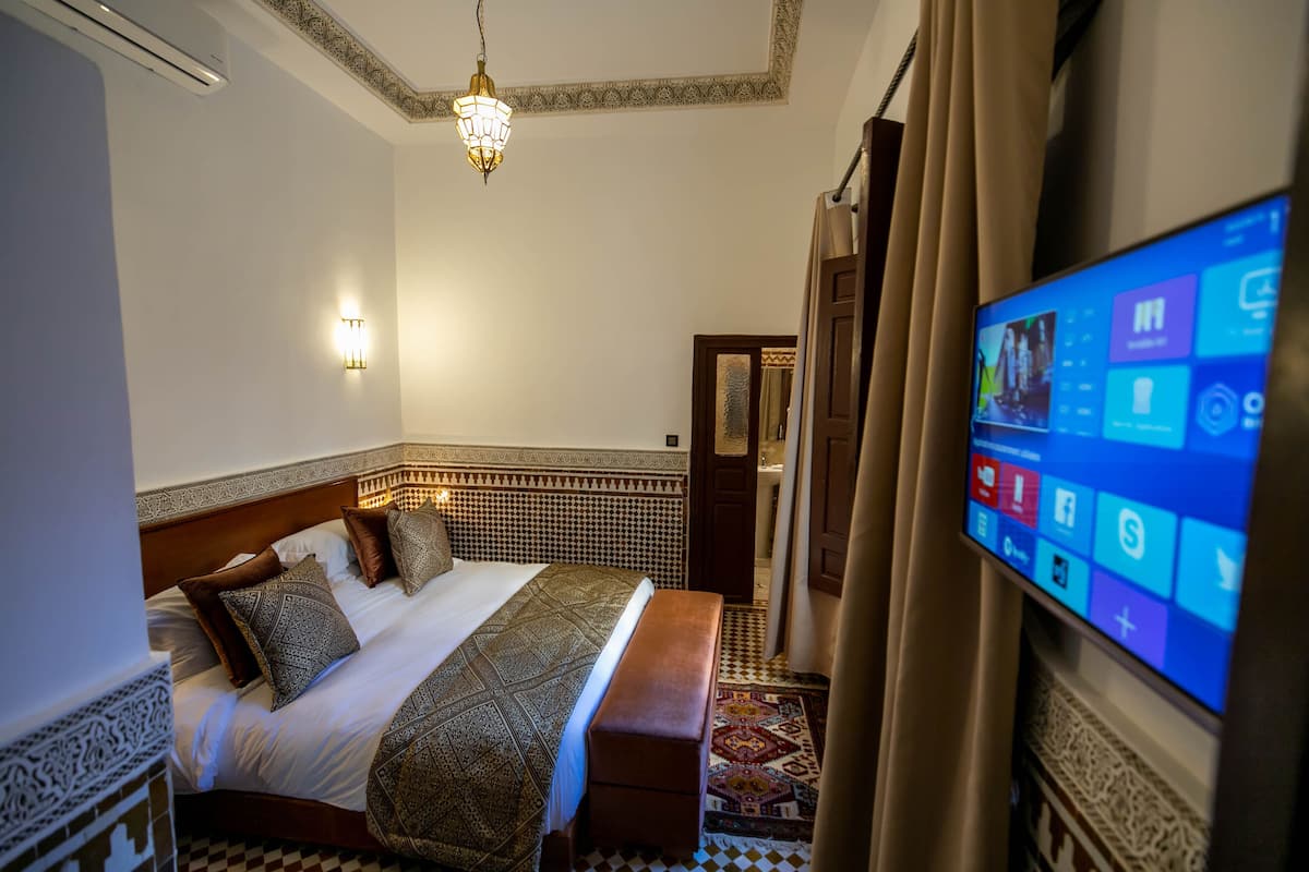 A hotel room with a large bed, a flat-screen TV, a patterned rug, and a decorative ceiling light.