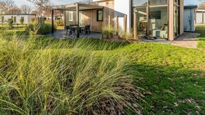A modern house with a glass facade, a patio with outdoor furniture, and a well-maintained lawn.